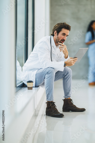A Worried Doctor Using Digital Tablet In A Hospital Hallway