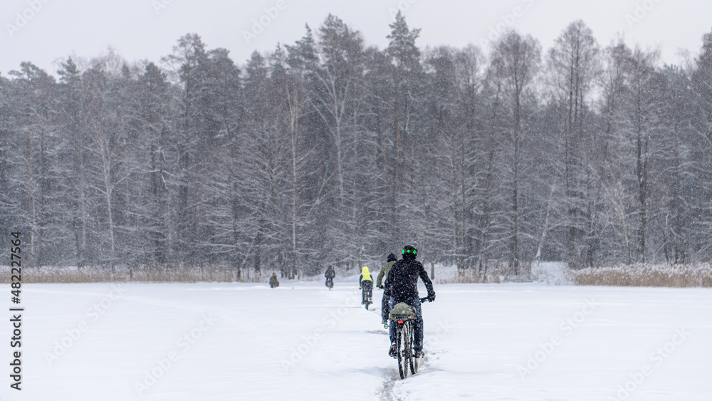 Russian bicyclists on winter lake with forest on background, Moscow Region
