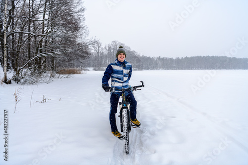 Russian bicyclist on winter lake with forest on background, Moscow Region