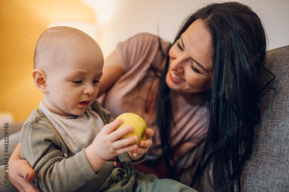 Mother playing with baby boy and eating a healthy food Mother playing with baby boy and eating a healthy food