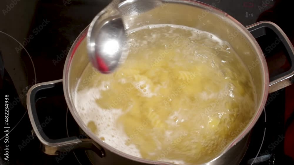Hand stirring raw pasta boiling in boiling water in a metal pot on the stove Hand stirring raw pasta boiling in boiling water in a metal pot on the stove