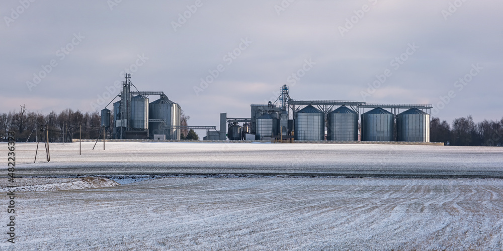 agro silos granary elevator in winter day in snowy field. Silos on agro-processing manufacturing plant for processing drying cleaning and storage of agricultural products, flour, cereals and grain. agro silos granary elevator in winter day in snowy field. Silos on agro-processing manufacturing plant for processing drying cleaning and storage of agricultural products, flour, cereals and grain.