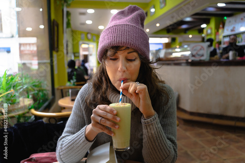 photo of pretty young woman with purple beanie enjoying a green smoothie in a coffee shop. Stock photography