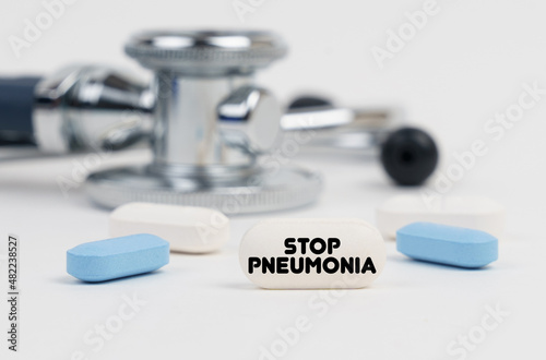 On a white surface lie pills, a stethoscope and a tablet with the inscription - STOP PNEUMONIA