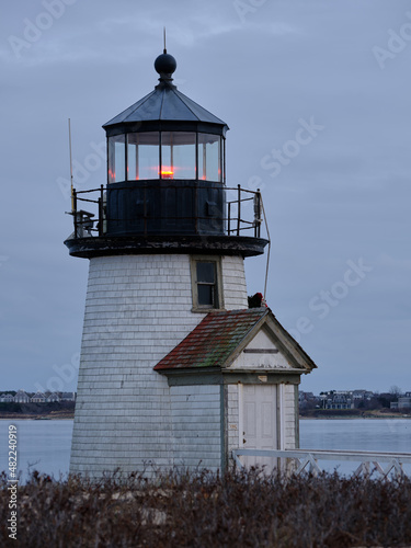 Vertical image of Dusk and sunset at the Brant Point Light house at the entrance to Nantucket Harbor on the island of Nantucket with tall seagrasses in the foreground