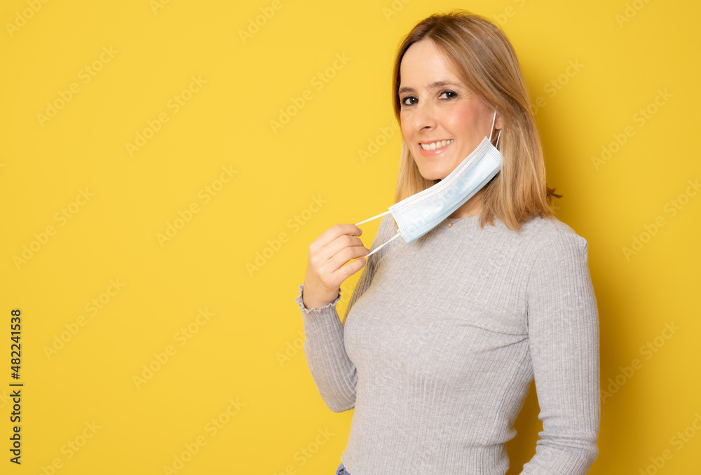 Portrait of satisfied woman putting on or taking off medical mask isolated over yellow background. Portrait of satisfied woman putting on or taking off medical mask isolated over yellow background.