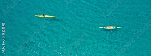 Aerial drone ultra wide panoramic photo with copy space of unidentified caucasian women paddling on tropical island exploring beautiful exotic nature in turquoise calm sea