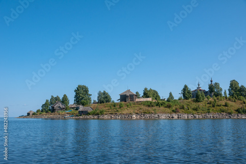 View of Church of Nativity of Virgin and old wooden sheds on shore of Lake Segozero in summer, Karelia, Russia