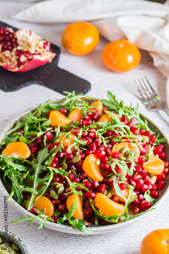 Fruit vitamin salad of pomegranate, tangerine, arugula and pumpkin seeds in a plate on the table. Organic vegetarian food.  Vertical view. Close-up