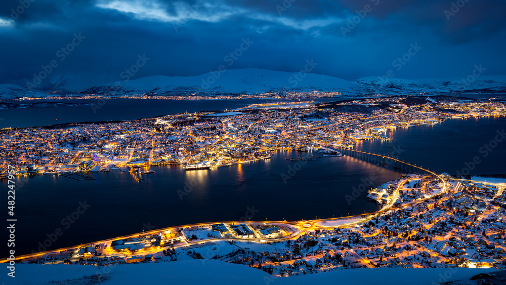 Fototapeta premium Panoramic view of Tromso, Norway, from Fjellheisen on mount Storsteinen at blue hour with pink illuminated clouds.