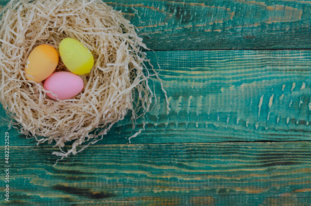 Multicolored eggs in a nest on a light green wooden background. Easter time. Top view.
