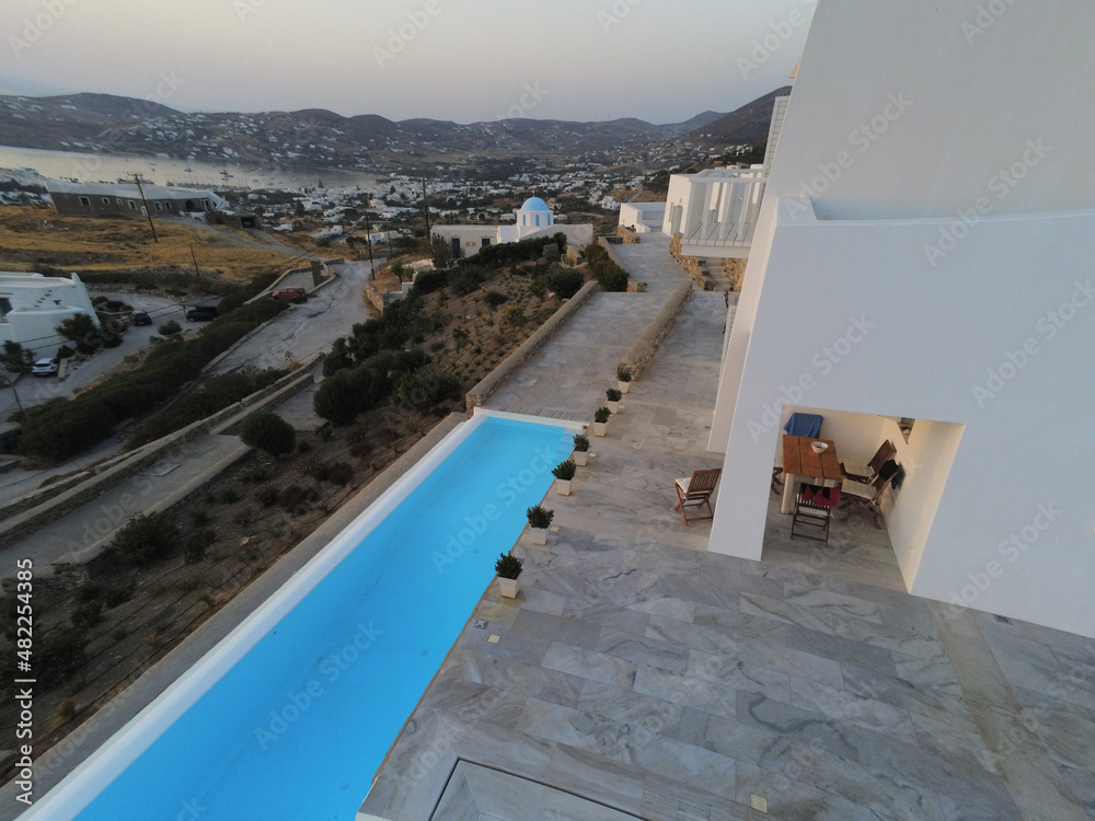 Aerial view of a luxurious greek house with swimming-pool. Typical greek church with blue roof and water bay in the background