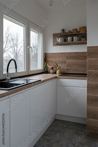 Modern kitchen interior with kitchen sink  wooden counter and design tiles on the wall. Sik near window in new apartment and white furniture in stylish interior. Vertical.