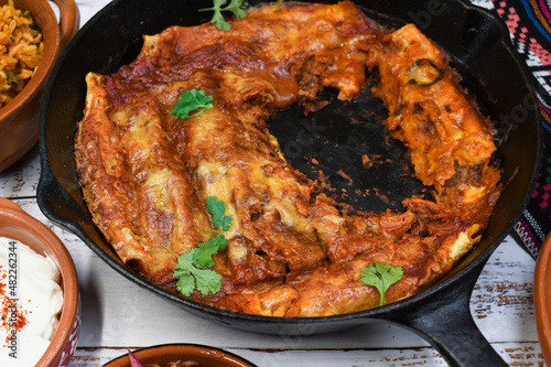 Bean enchiladas served in traditional cast iron skillet and clay dishes, white wooden table