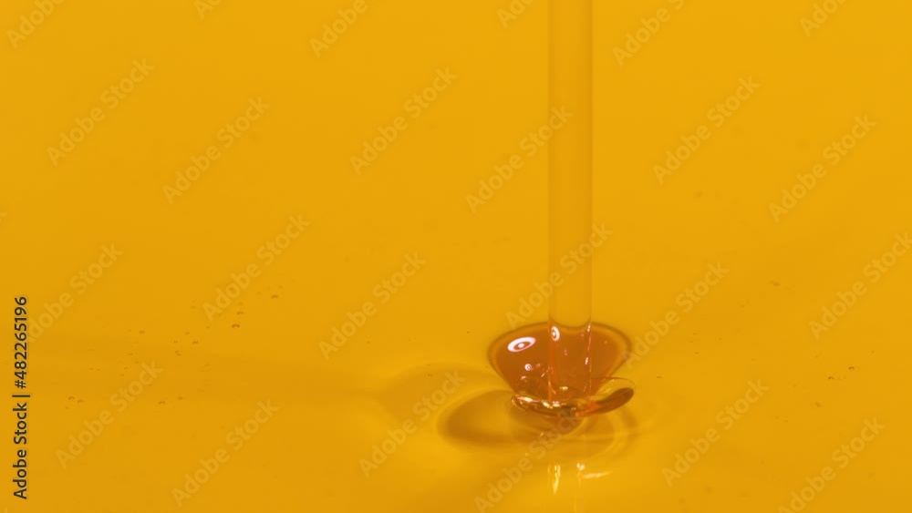 SLOW MOTION MACRO, DOF: Golden liquid falls into a container full of cold pressed extra virgin olive oil. Shiny unrefined avocado oil streams into a full dish. Organically grown cooking ingredient.