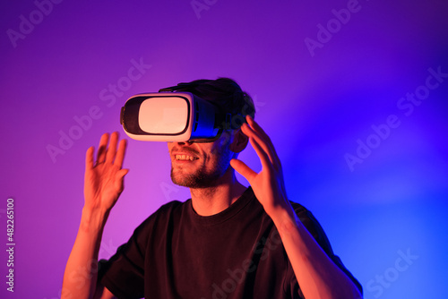 Man using VR virtual reality glasses. Futuristic metaverse universe games and future in digital technology. Entreatment and NFT in neon colorful space. Happy male. Slow motion video in 3d cyber space. © Girts