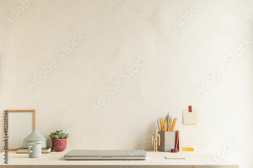 Home office, creative desk with office supplies and beige wall.