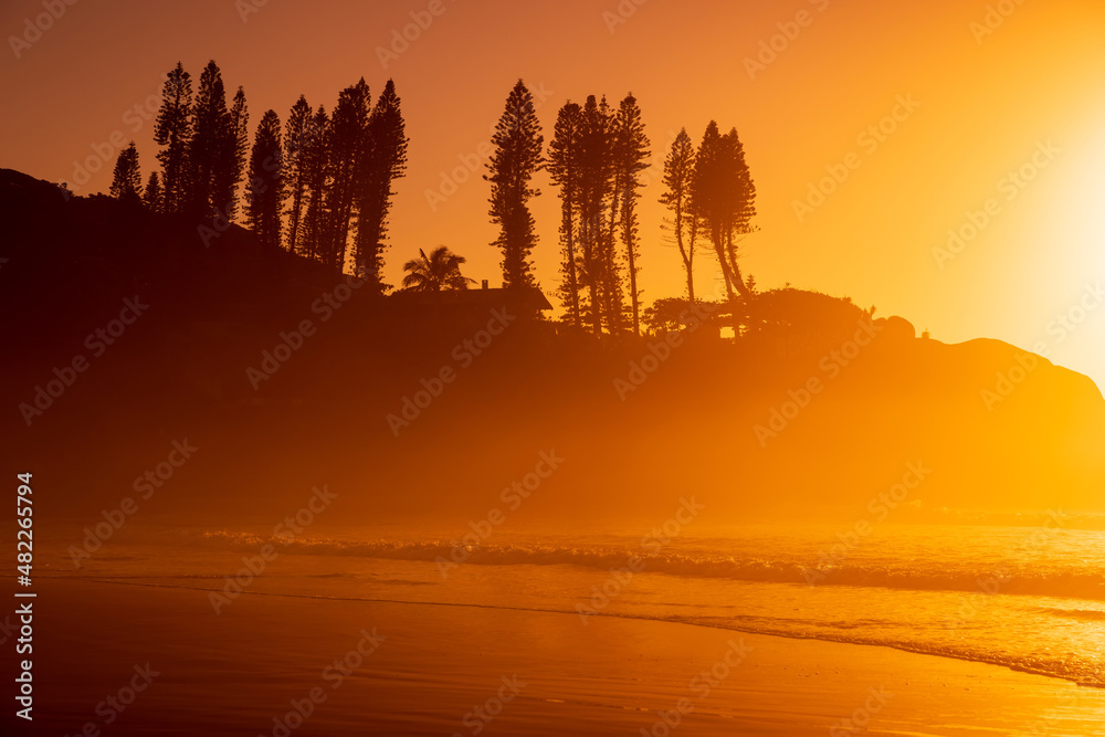 Bright sunrise with waves and rocks with trees. Joaquina beach in Brazil