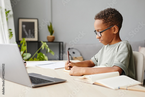 Side view portrait of African-American boy studying at home with laptop open, homeschooling concept
