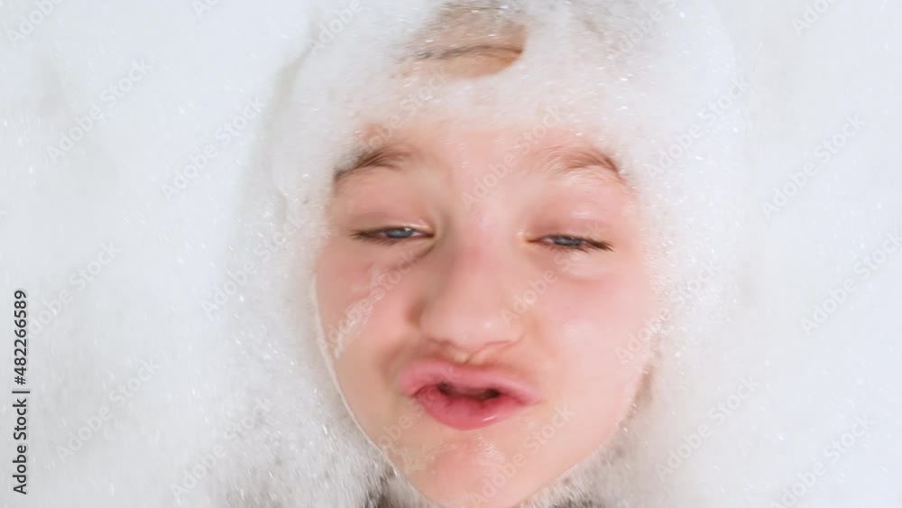 Portrait of cheerful teen girl lying in bath with thick soap foam and looking in camera. Concept of child hygiene and health care at home. Child having fun and playing at home. Portrait of cheerful teen girl lying in bath with thick soap foam and looking in camera. Concept of child hygiene and health care at home. Child having fun and playing at home.