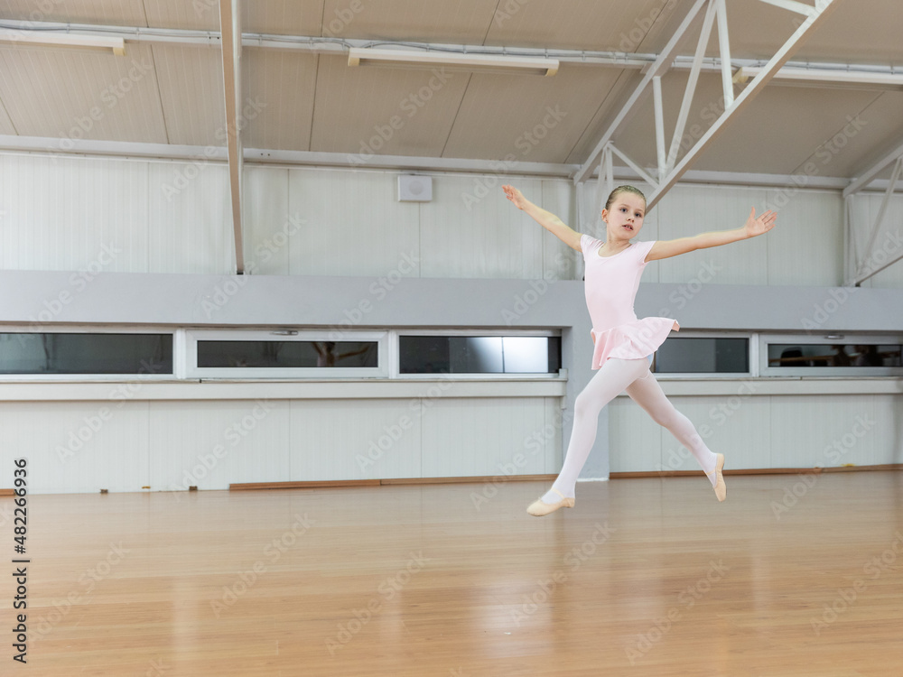 Fototapeta premium Young ballerina performing jump in ballet studio