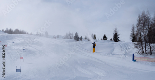 artificial snow slope with snow cannon in operation making a snow cloud on the ski run in the mountains