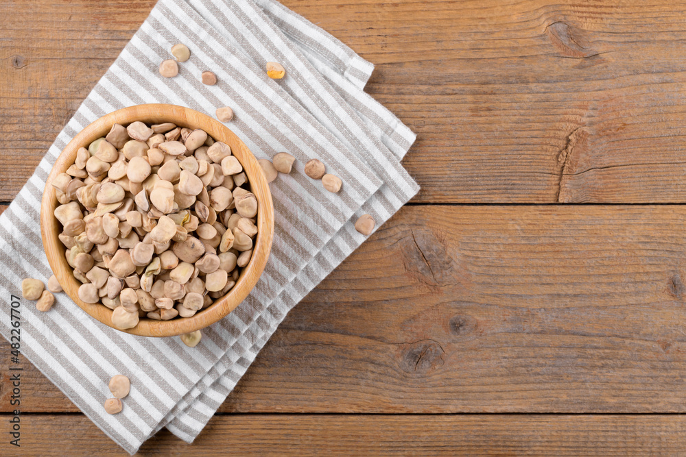 Dry raw cicerchia or indian pea on a wooden bowl with napkin on natural wooden background, top view, copy space. Legumes known as Lathyrus Sativus, Chickling Vetch, Blue Sweet Pea, made in Puglia Dry raw cicerchia or indian pea on a wooden bowl with napkin on natural wooden background, top view, copy space. Legumes known as Lathyrus Sativus, Chickling Vetch, Blue Sweet Pea, made in Puglia