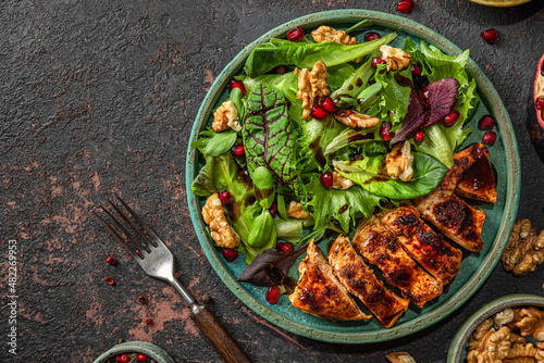 Grilled chicken breast fillet and mix salad with walnuts, pomegranate and balsamic sauce on dark background