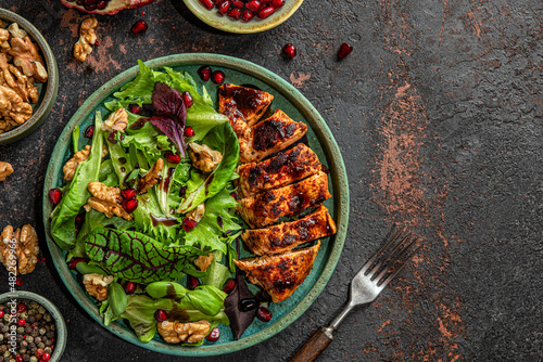 Fresh salad with grilled chicken fillet, mix greens, walnuts, pomegranate and balsamic sauce on black background