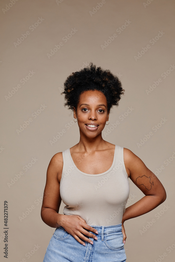 Vertical waist up portrait of young African-American woman smiling at camera while standing against neutral background, natural beauty Vertical waist up portrait of young African-American woman smiling at camera while standing against neutral background, natural beauty