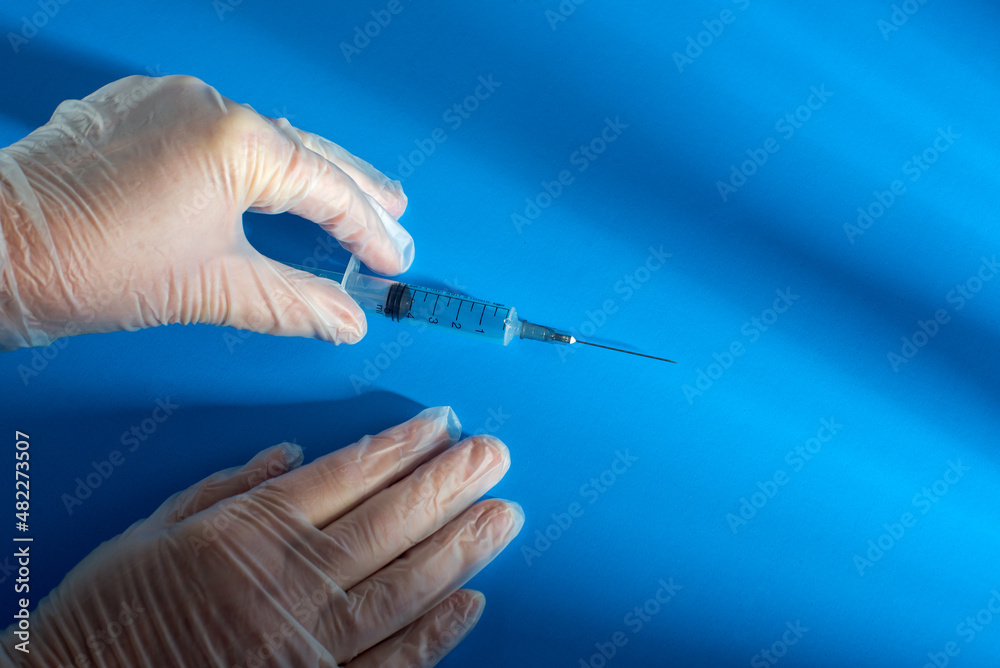 gloved hands take a plastic syringe with liquid for injection, on a blue background. Health care, treatment concept. gloved hands take a plastic syringe with liquid for injection, on a blue background. Health care, treatment concept.