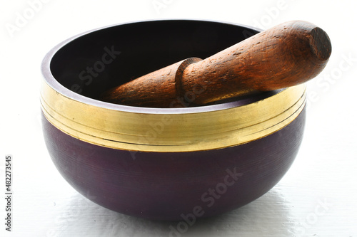A close up image of a purple meditation singing bowl with wooden mallet on a white background. 