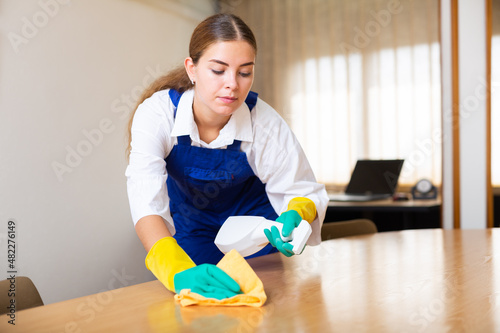 Concentrated young woman worker from a cleaning company cleans the table with a rag and detergent © JackF