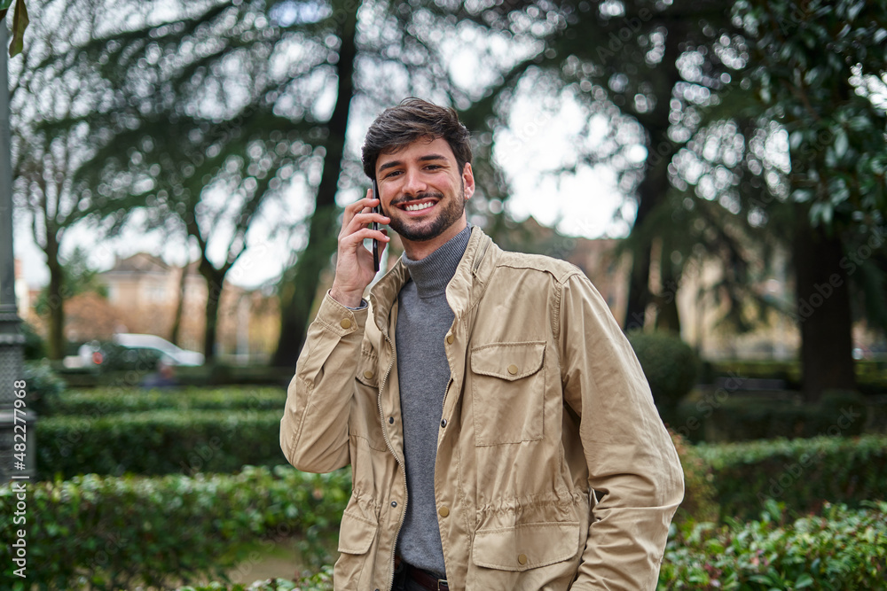 Smiling man talking on smartphone while walking in park Smiling man talking on smartphone while walking in park
