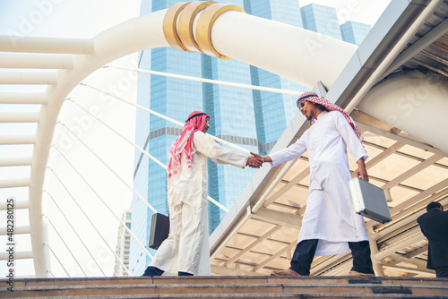 Arab Businessman Muslim dress shaking hands together in modern city UAE background. Muslim Men Teamwork business partner handshake with Partnership. diversity multiracial arab people trust commitment