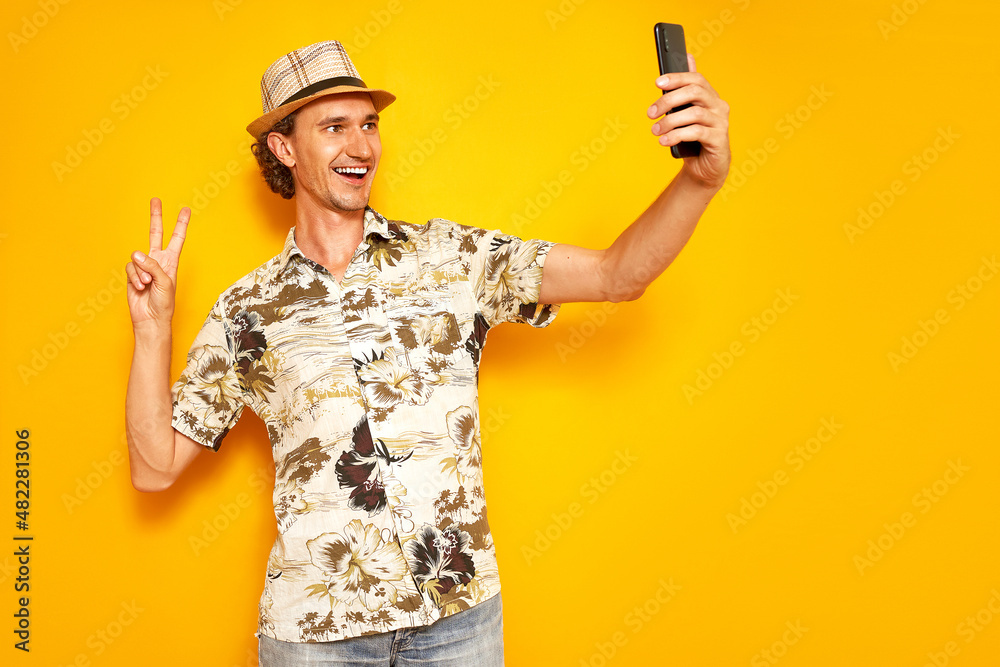 happy male tourist traveler with phone in his hand takes selfie, communicates via video communication on voyage on vacation. isolated on yellow background. concept - people, technology, communication