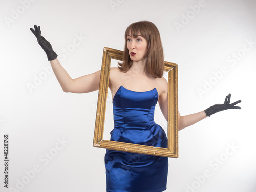 Art portrait of a woman. Girl in a blue evening dress. She has a large picture frame around her neck. Creative woman on a white background. Studio portrait of a creative woman.