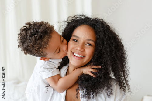 Loving young african American mother hugging cute baby, son. Smiling mom playing with little child toddler at home. Childcare concept. Woman and kid enjoy family time together