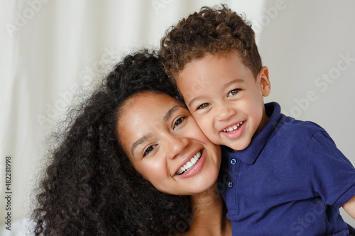 Loving young african American mother hugging cute baby, son.  Smiling mom playing with little child toddler at home. Childcare concept. Woman and kid enjoy family time together