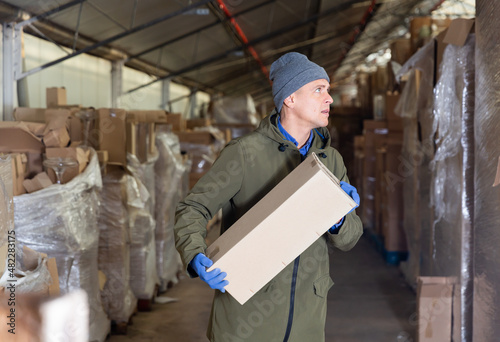 Storekeeper man stacking pasteboard box in storehouse during working day.