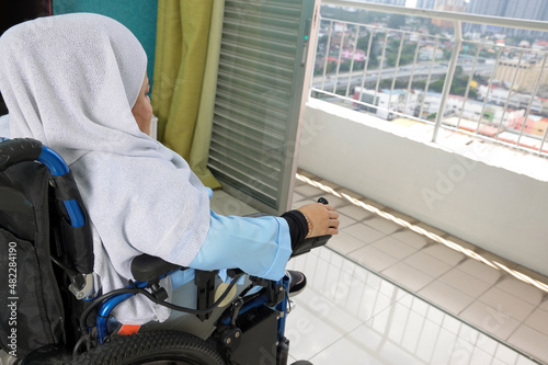 South east Asian malay headscarf tudung middle aged disabled woman on wheelchair looking sitting in front of balcony window look outside closeup hand