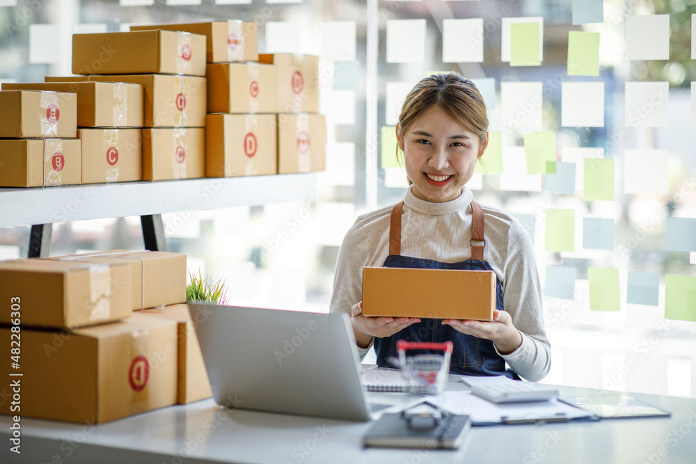 Startup SME small business entrepreneur SME or freelance Asian woman using a laptop with box, Young success Asian woman with her hand lift up, online marketing packaging box and delivery, SME concept. Startup SME small business entrepreneur SME or freelance Asian woman using a laptop with box, Young success Asian woman with her hand lift up, online marketing packaging box and delivery, SME concept.