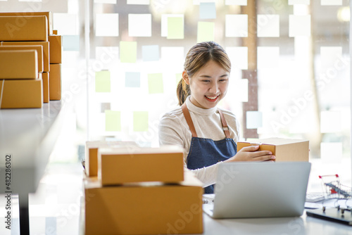Startup SME small business entrepreneur SME or freelance Asian woman using a laptop with box, Young success Asian woman with her hand lift up, online marketing packaging box and delivery, SME concept.