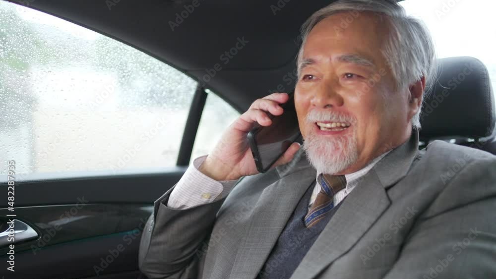 Confidence senior businessman in suit sitting on car back seat using mobile phone talking with business partner while going to office. Elderly CEO working in automobile and looking out of the window Confidence senior businessman in suit sitting on car back seat using mobile phone talking with business partner while going to office. Elderly CEO working in automobile and looking out of the window