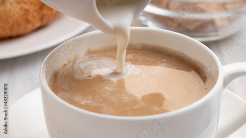 Pouring milk or cream into freshly brewed coffee, close up