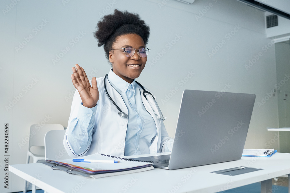 Smiley young female nurse in medical uniform sit at desk has videocall on laptop Smiley young female nurse in medical uniform sit at desk has videocall on laptop