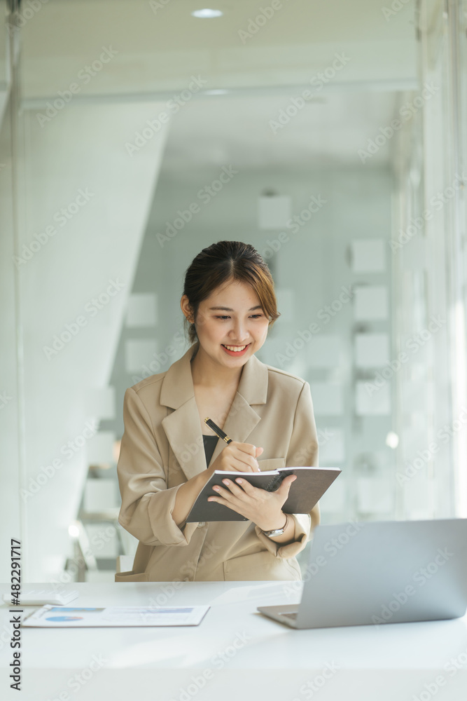 Young asian woman taking note and using laptop while studying at home,woman relaxing in the living room at home, she is using a laptop,online learning concept via laptop computer. Young asian woman taking note and using laptop while studying at home,woman relaxing in the living room at home, she is using a laptop,online learning concept via laptop computer.