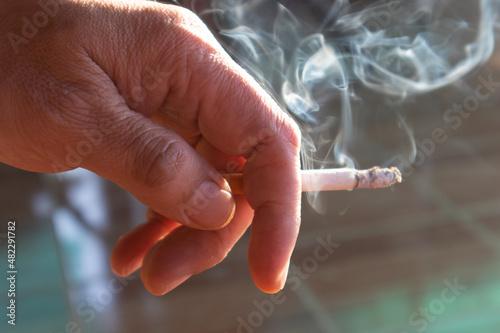 Selective focus hand holding a cigarette with the smoke