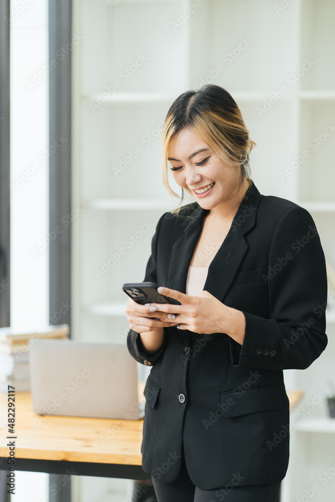 Successful young business woman using a smartphone while standing in front of her own business office. Concept of the start-up business Successful young business woman using a smartphone while standing in front of her own business office. Concept of the start-up business