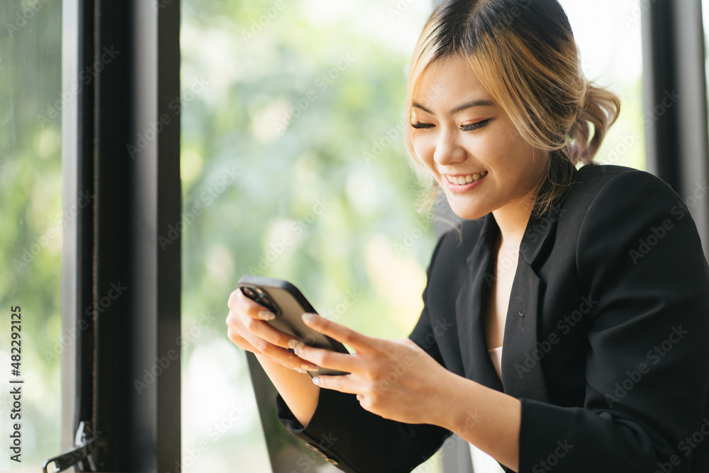 Portrait of a cheerful asian woman looking at the street while sitting in a coffee shop with a mobile phone in her hands. Business woman happy to read good news on a smartphone form business partners Portrait of a cheerful asian woman looking at the street while sitting in a coffee shop with a mobile phone in her hands. Business woman happy to read good news on a smartphone form business partners